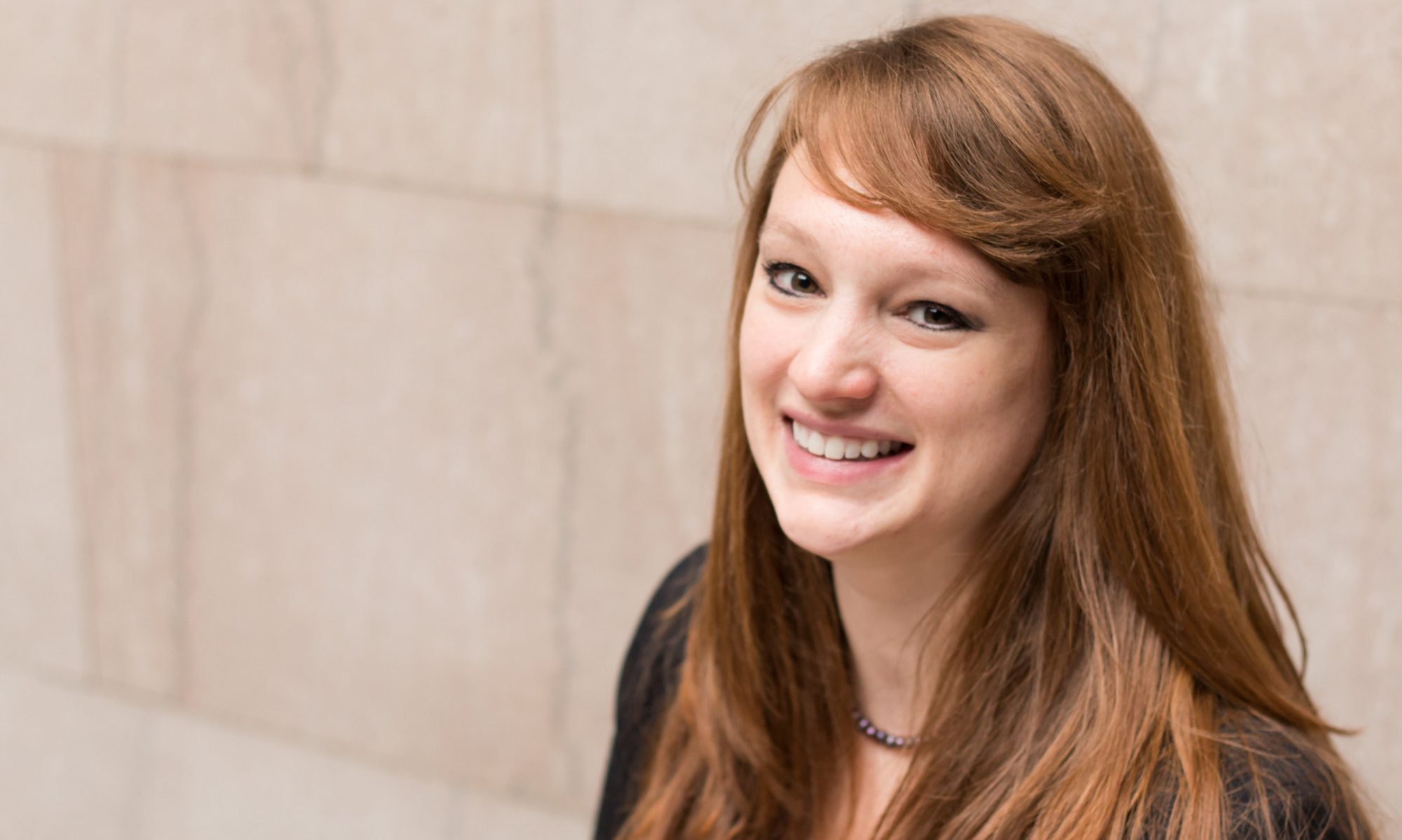 Caitlin smiles into the camera against a marble wall.